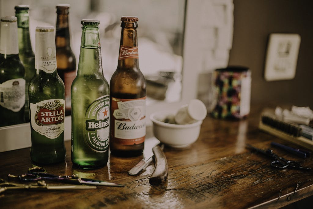 Beer bottles and barber tools on a wooden barbershop counter with a blurred mirror reflection.